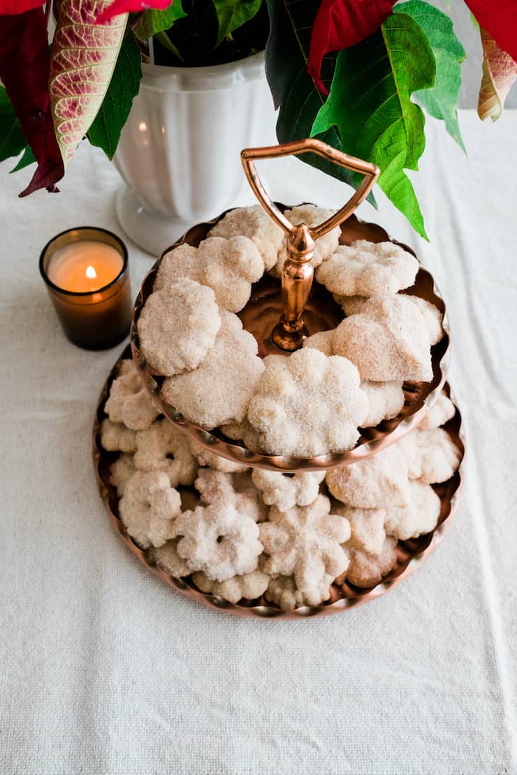 Biscochos Mexican wedding cookies on a brass dessert stand with a poinsettia and candle in the background