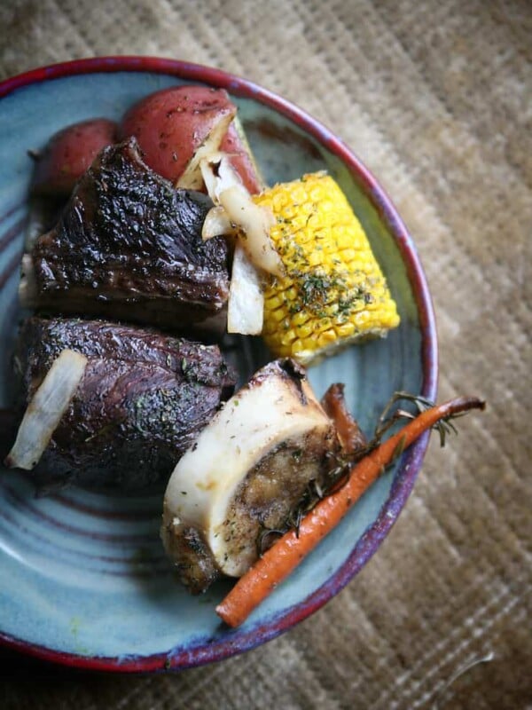 Mexican beef short ribs recipe by Yvette Marquez-Sharpnack of Muy Bueno served with potatoes, carrots, corn, and marrow bone on a rustic plate