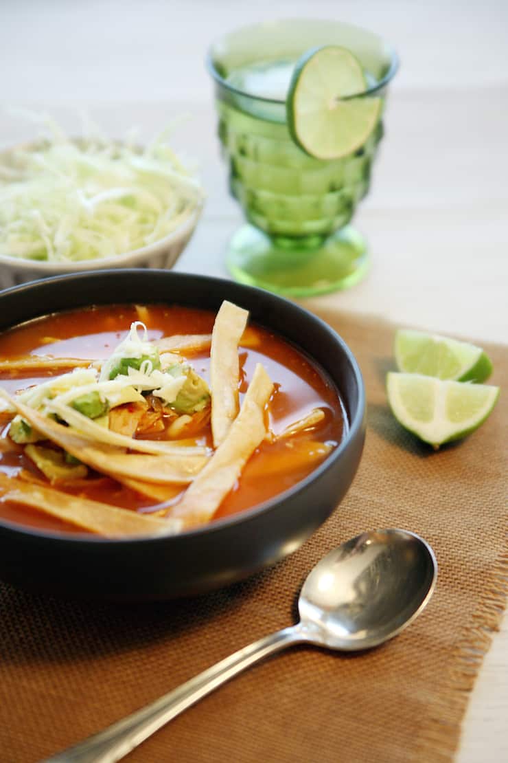 Chicken tortilla soup served in a black bowl topped with tortilla strips