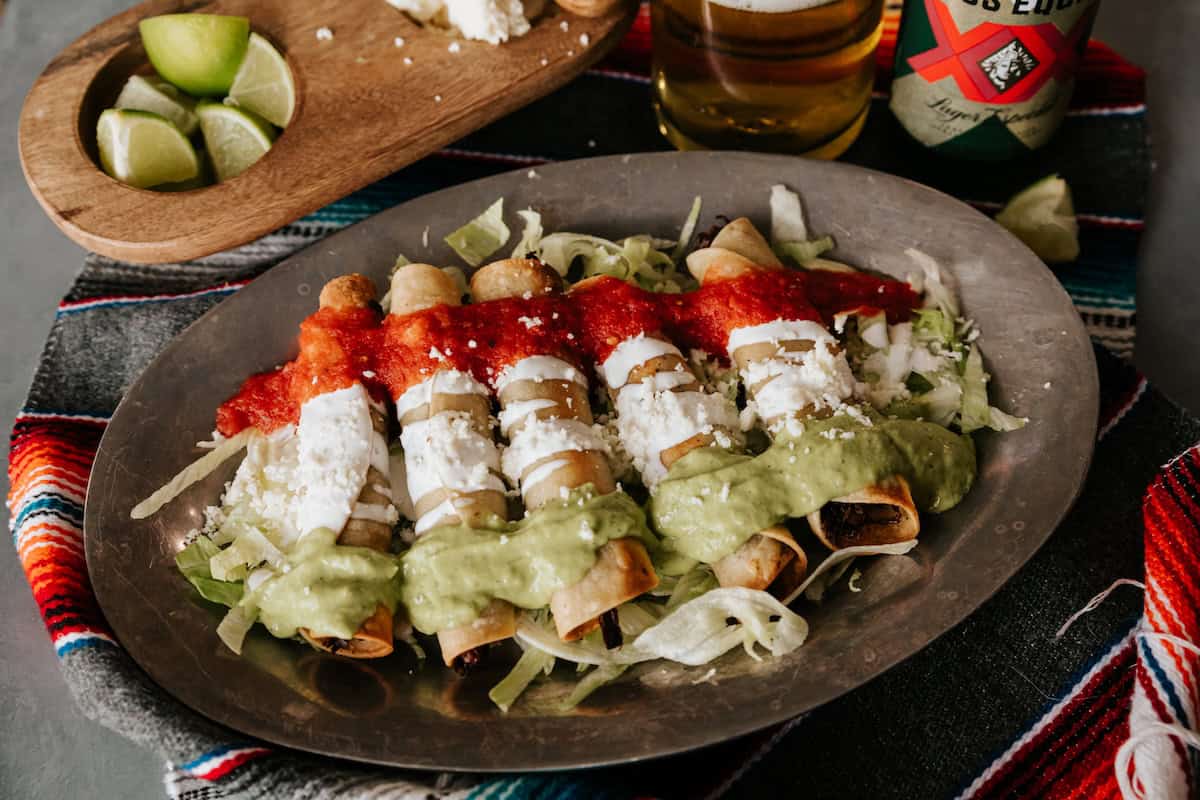 Crispy brisket flautas with green avocado tomatillo salsa, Mexican crema, and red tomato broth for a Mexican flag presentation.