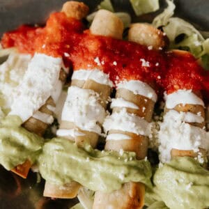 Brisket Flautas Banderas topped with avocado tomatillo salsa, Mexican crema, and tomato broth.