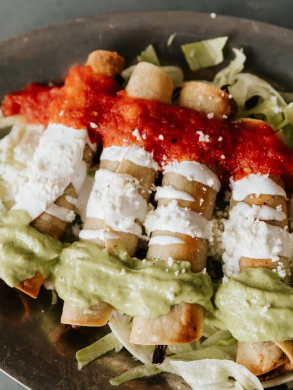 Brisket Flautas Banderas topped with avocado tomatillo salsa, Mexican crema, and tomato broth.