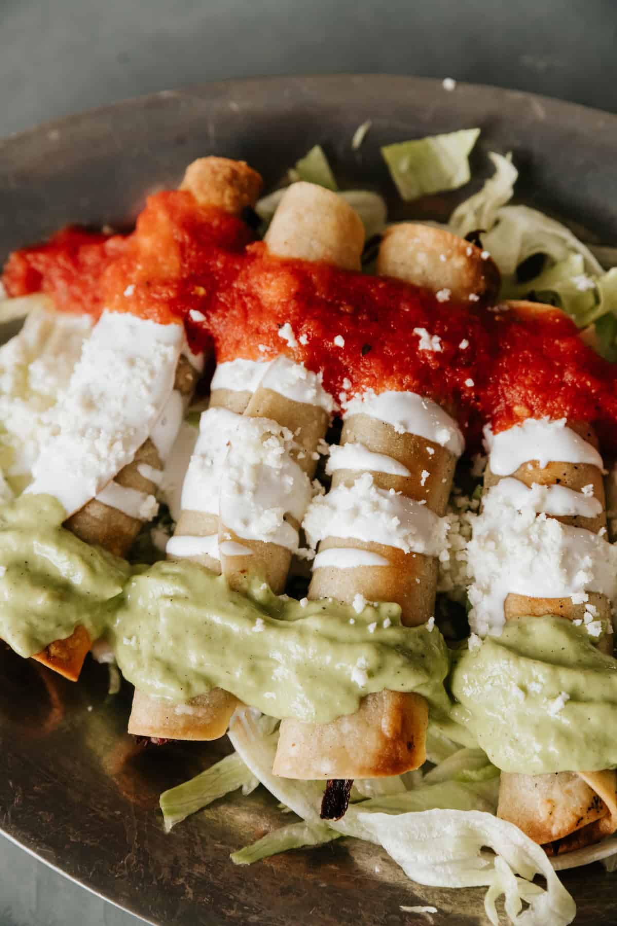 Brisket Flautas Banderas topped with avocado tomatillo salsa, Mexican crema, and tomato broth.