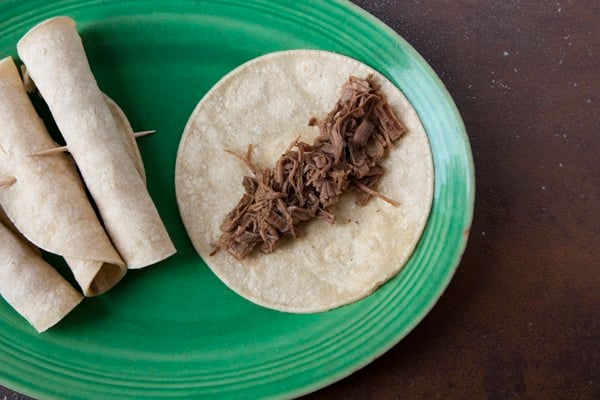 filling corn tortillas with shredded brisket flautas