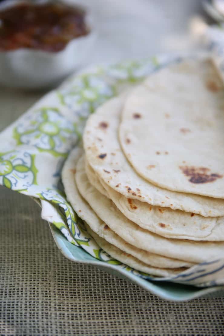 A stack of Homemade Flour Tortillas on a plate lined with a cloth