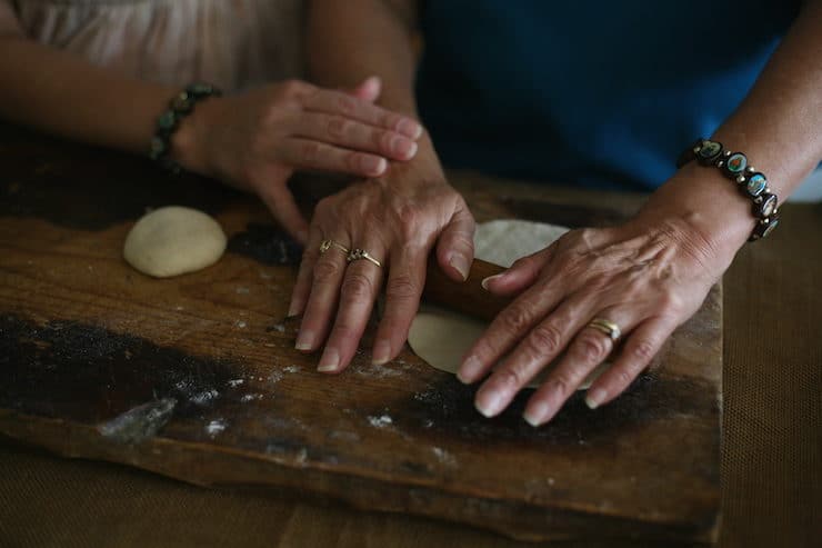 Mother and daughter hands making homemade flour tortillas with a small wooden rolling pin