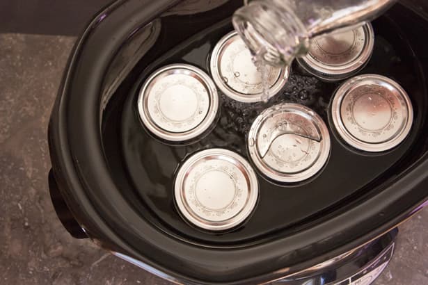 jars filled with condensed milk in slow cooker with water.