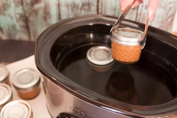 tongs holding a jar of homemade dulce de leche out of slow cooker.