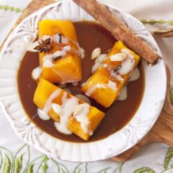 Mexican candied pumpkin on a white dish with brown sugar syrup, a cinnamon stick and drizzled with sweetened condensed milk