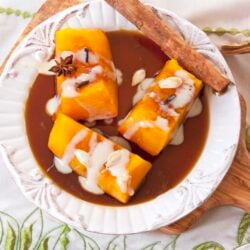 Mexican candied pumpkin on a white dish with brown sugar syrup, a cinnamon stick and drizzled with sweetened condensed milk