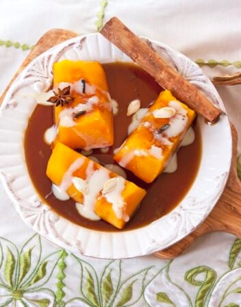 Mexican candied pumpkin on a white dish with brown sugar syrup, a cinnamon stick and drizzled with sweetened condensed milk