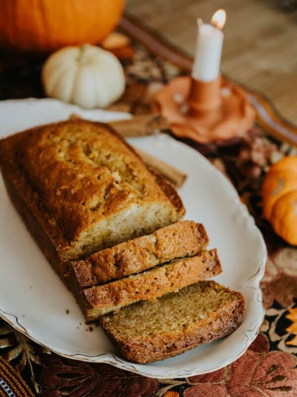 Sliced Mexican pumpkin bread on a white platter with pumpkins in the background.