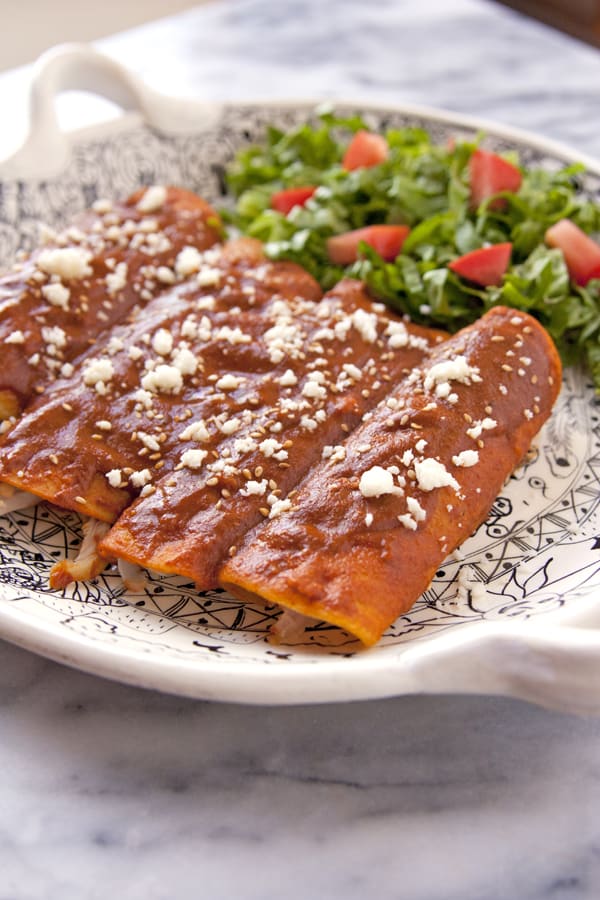 chicken mole enchiladas on a Mexican black and white platter with a side salad