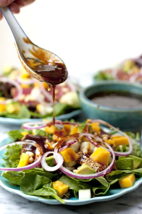 spoon drizzling tangy and salty dressing over a seared ahi tuna salad with avocado and mango