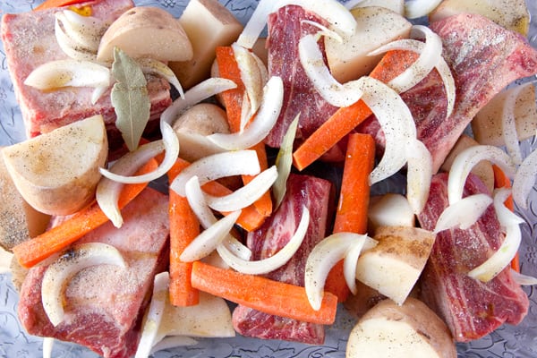 beef short ribs in a glass casserole dish with onions carrots and potatoes