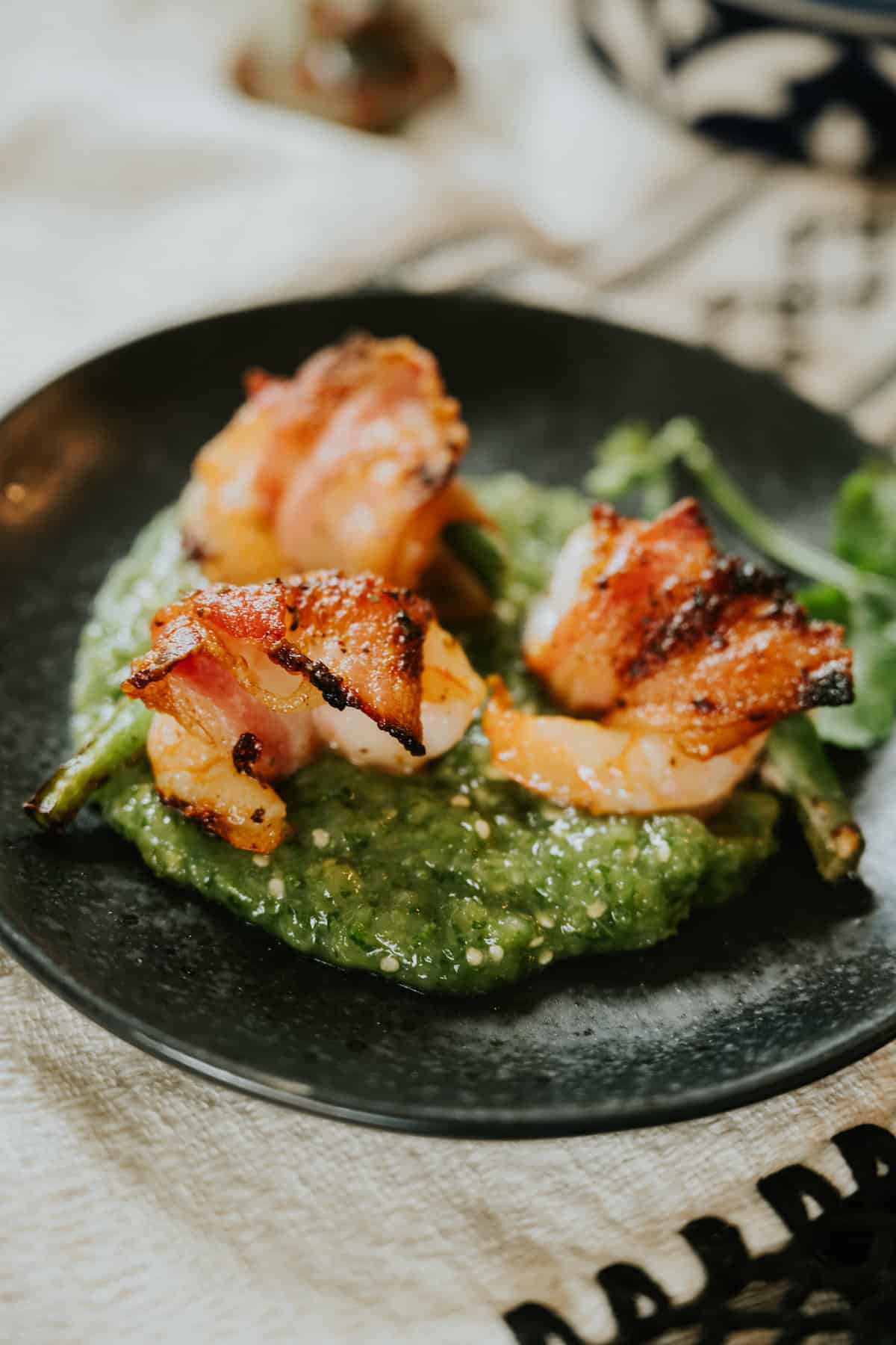 Bacon-Wrapped Shrimp with Jalapeño served on salsa verde on a black plate.