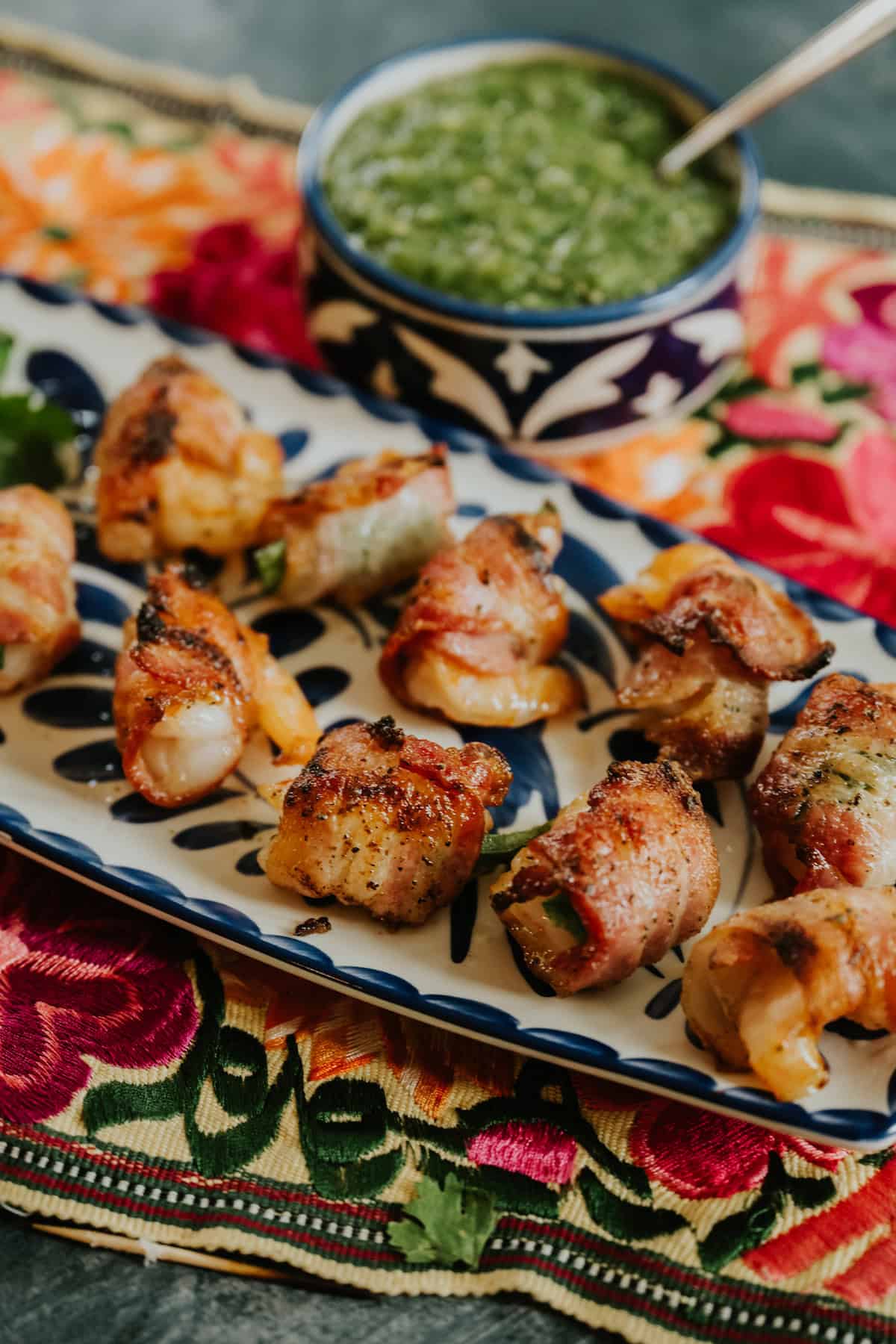 Bacon-Wrapped Shrimp with Jalapeño on a colorful platter with a bowl of salsa verde.