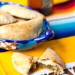 Baked Hatch green chile and cheese empanadas in a colorful Mexican dish, with one empanada broken open to show the cheesy chile filling.