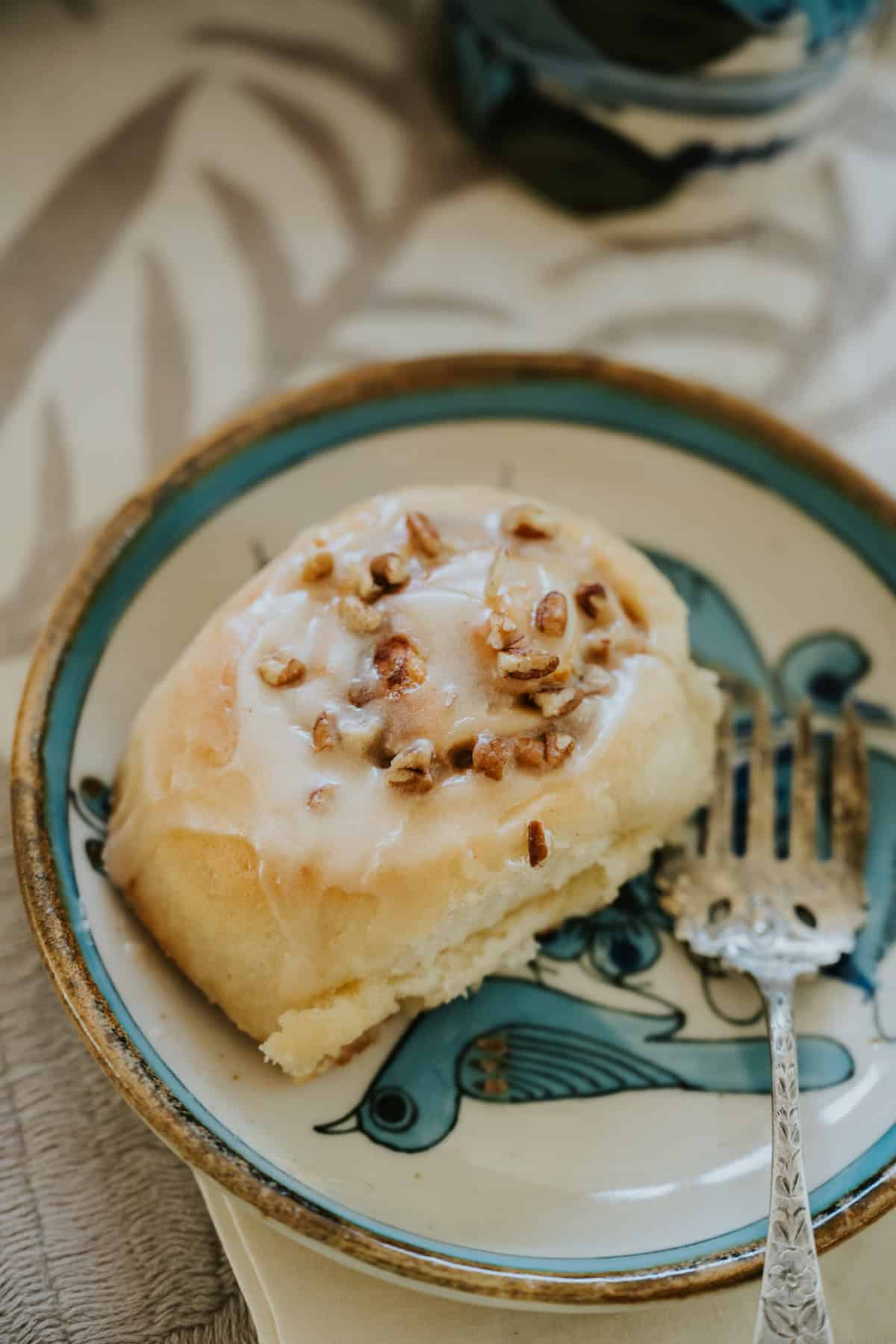 Close-up of a glazed dulce de leche cinnamon roll topped with chopped pecans on a decorative ceramic plate.
