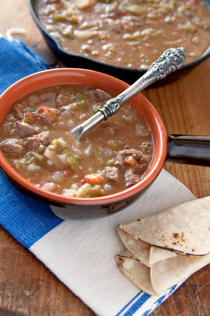 small bowl filled with a green Chile stew with a side of corn tortillas - Chile Verde con Carne y Papas (Green Chile with Beef and Potatoes)