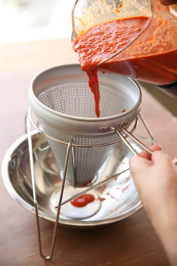 tipping red Chile sauce from a blender into a chinois to strain.