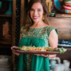 Latina food blogger holding a serving platter of pork tinga flautas to serve for a cinco de mayo party.