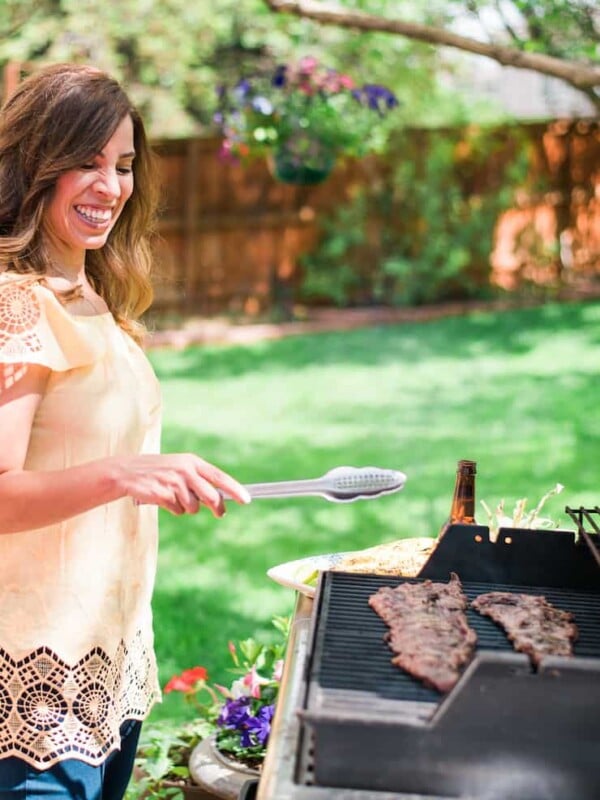 Yvette Marquez Muy Bueno grilling steak on a grill outside the house with a big tree blurred in the background