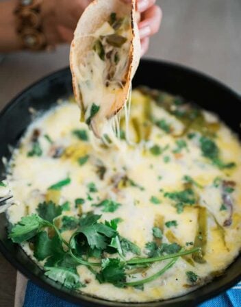 hand holding tortilla filled with queso fundido with hatch chiles and mushrooms