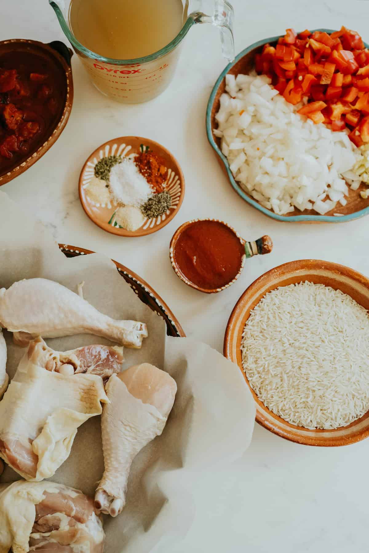 Ingredients for Arroz con Pollo including chicken, rice, broth, tomatoes, onion, and spices laid out on a table.