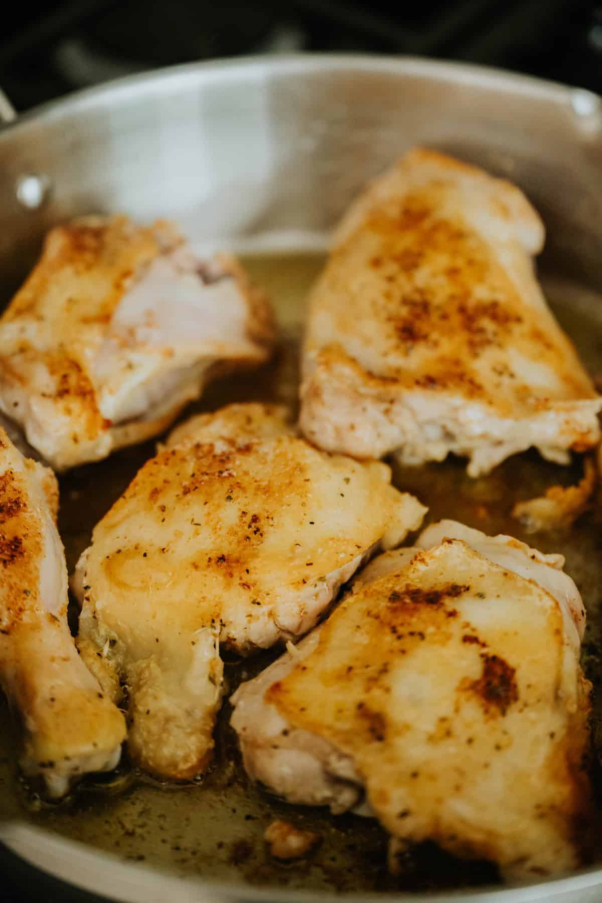 Bone-in chicken thighs browning in a skillet until golden.