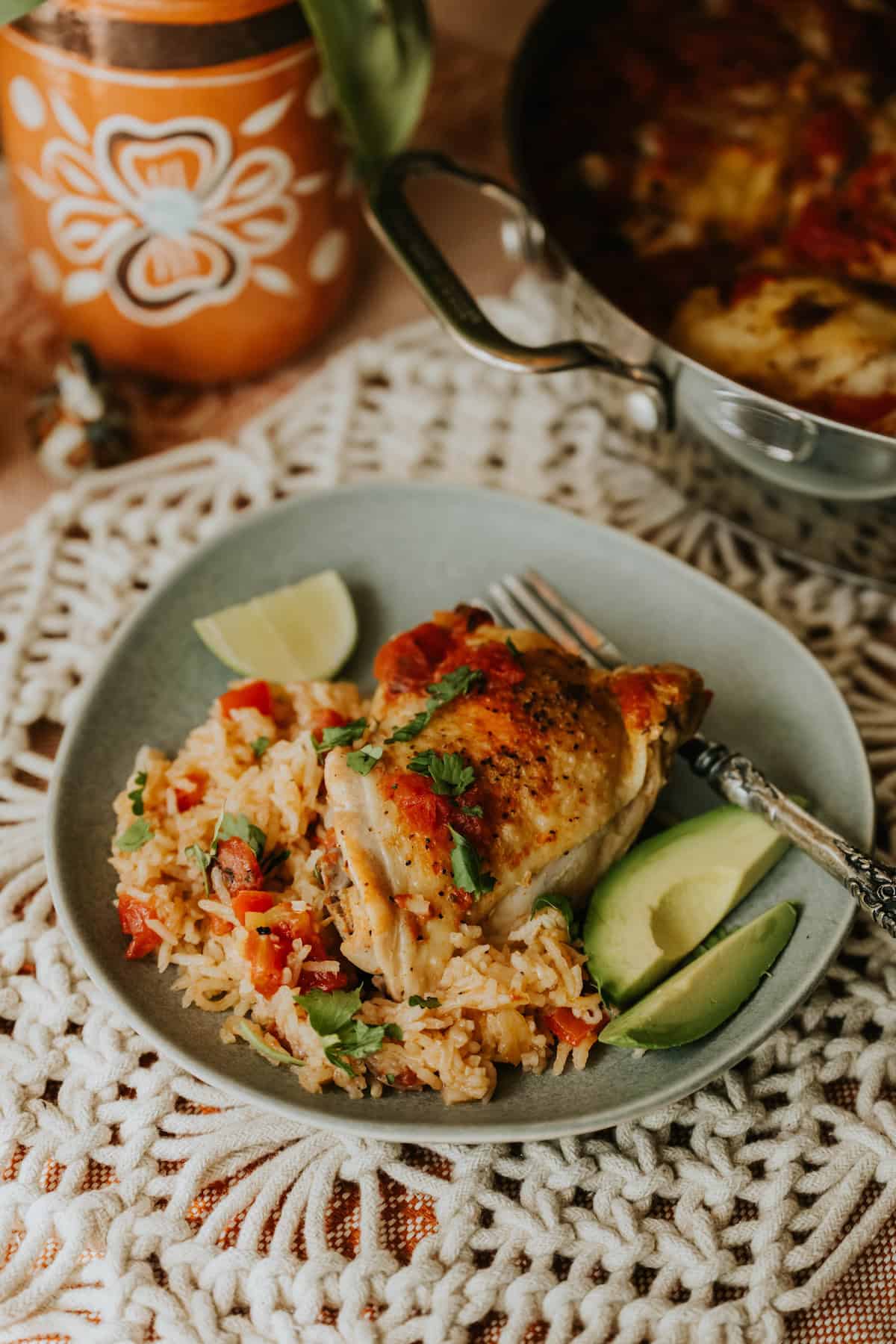Bowl of Arroz con Pollo topped with cilantro and avocado slices on a lace tablecloth.