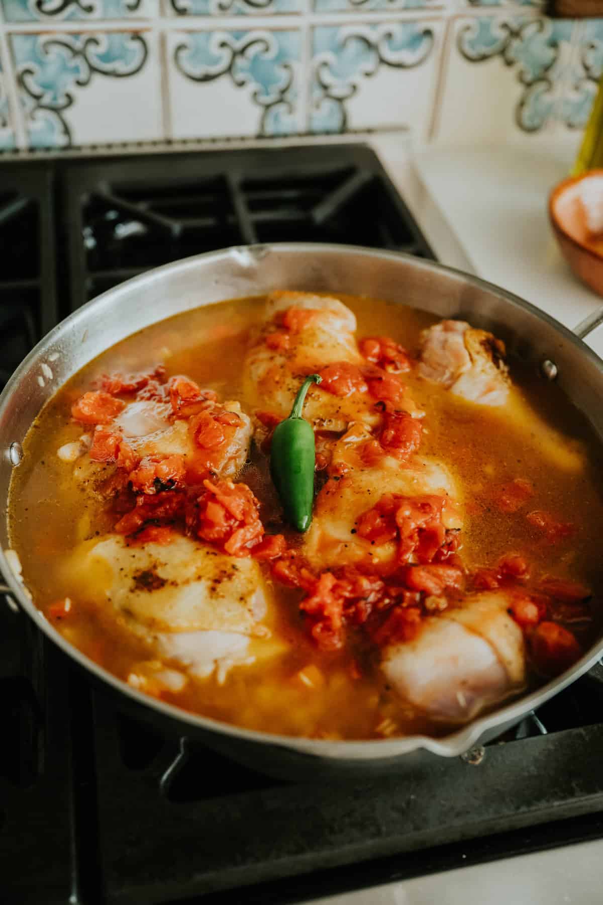 One-pan Arroz con Pollo cooking on the stove with chicken, rice, and a jalapeño on top.