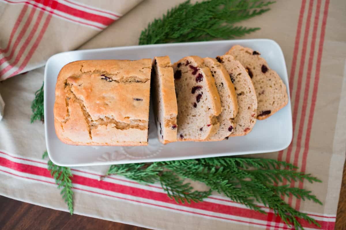 Freshly baked Cranberry Walnut Bread on a holiday table with evergreen sprigs and a red striped napkin.