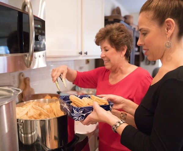 Latina women mother and daughter in the kitchen making tamales at a tamalada.