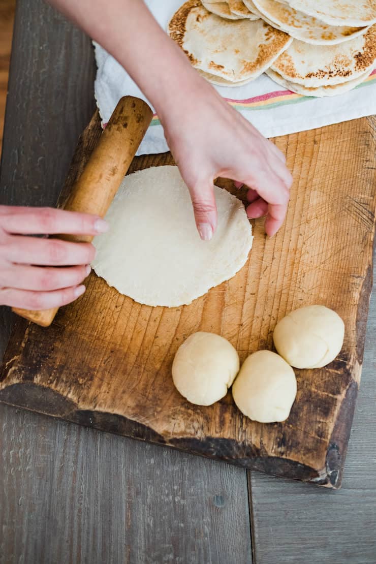 hands rolling out gordita dough with a wooden rolling pin.