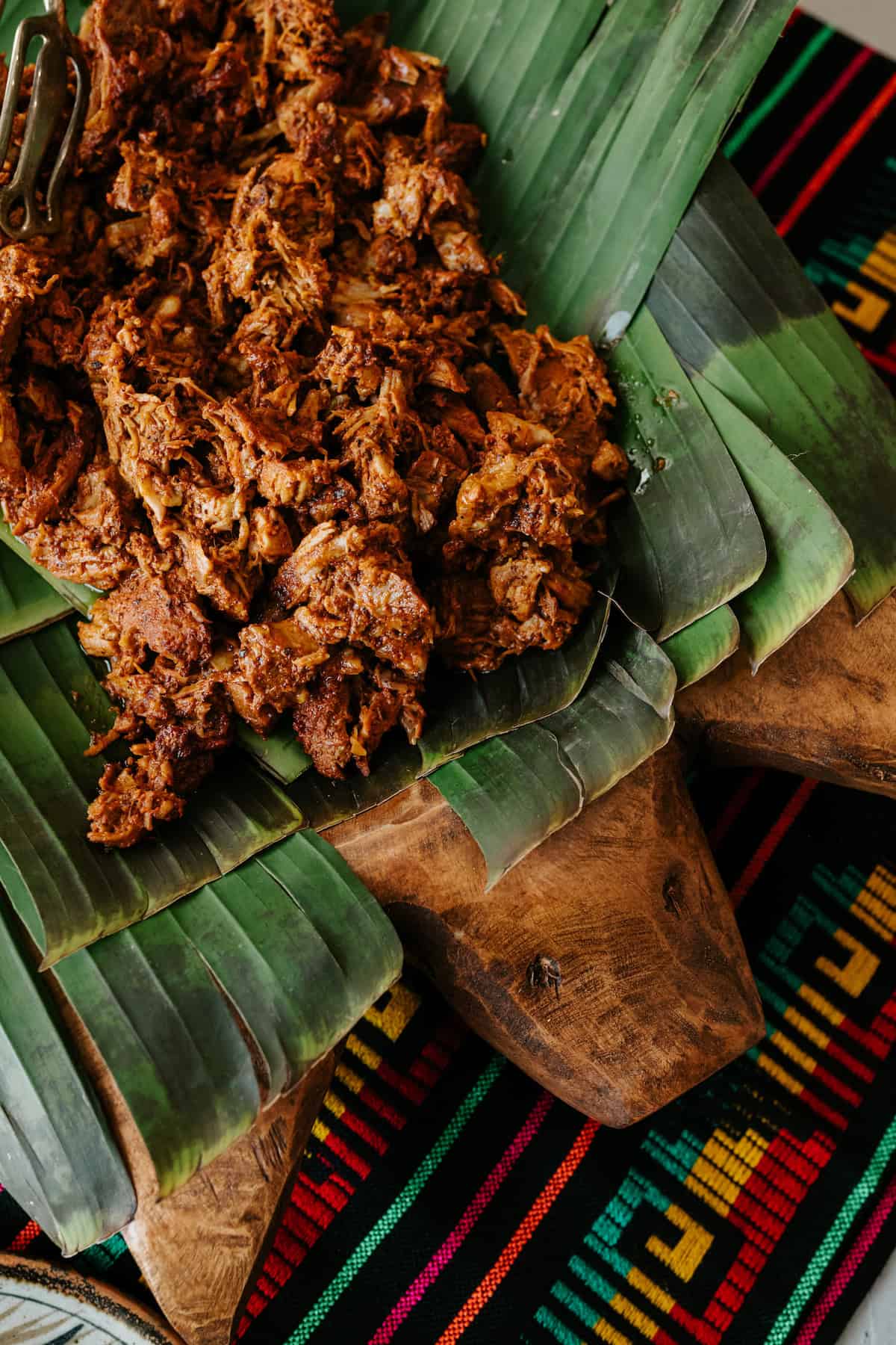 Shredded Cochinita Pibil served on banana leaves atop a wooden pig platter, showcasing its deep red-orange color and tender texture.