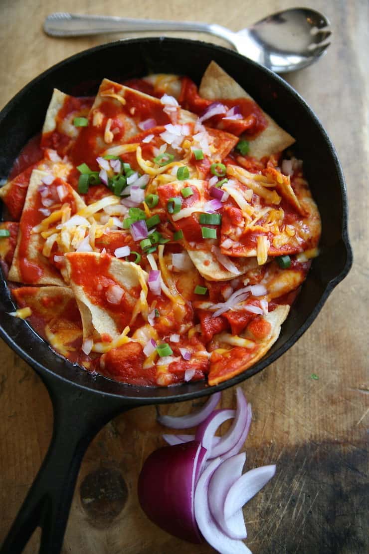 red chile chilaquiles in a cast iron pan topped with green and red onions 