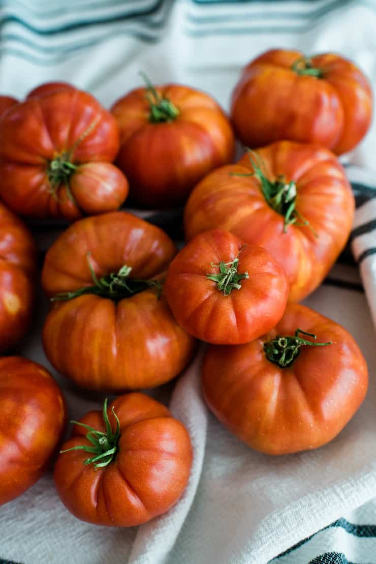 pile of farm fresh heirloom tomatoes on a white tea towel with a black stripe