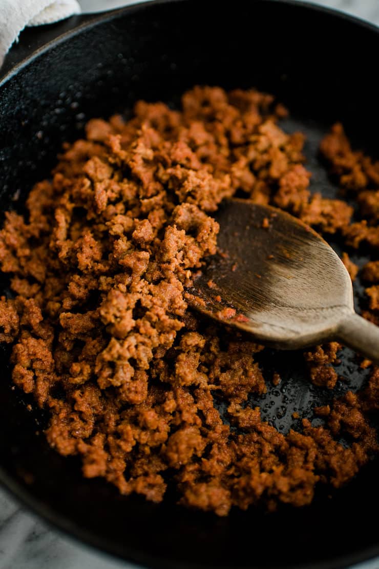 mexican chorizo being cooked in a cast iron skillet with a wooden spoon