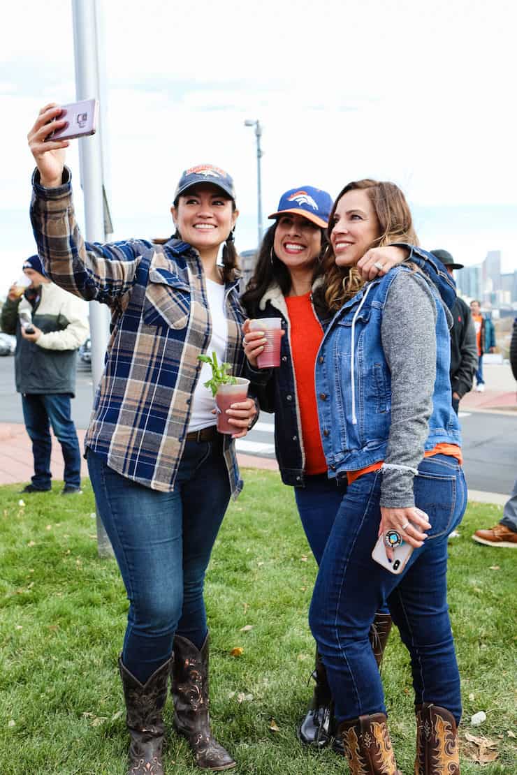 three Latina girls taking a selfie at a Denver broncos tailgate holding Bloody Marys 