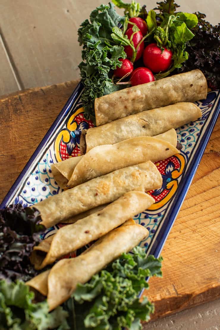 Crispy brisket flautas made with corn tortillas arranged on a colorful Mexican platter.