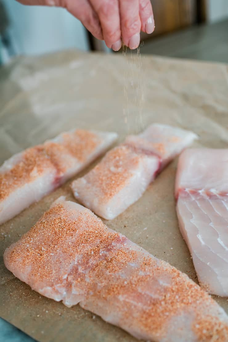Applying dry taco spice rub on tilapia fillet by sprinkling from a height.