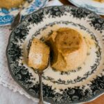 Overhead shot of individual Mexican coffee flans (flan café de olla) served on vintage floral plates with caramel sauce and a spoon on the side.