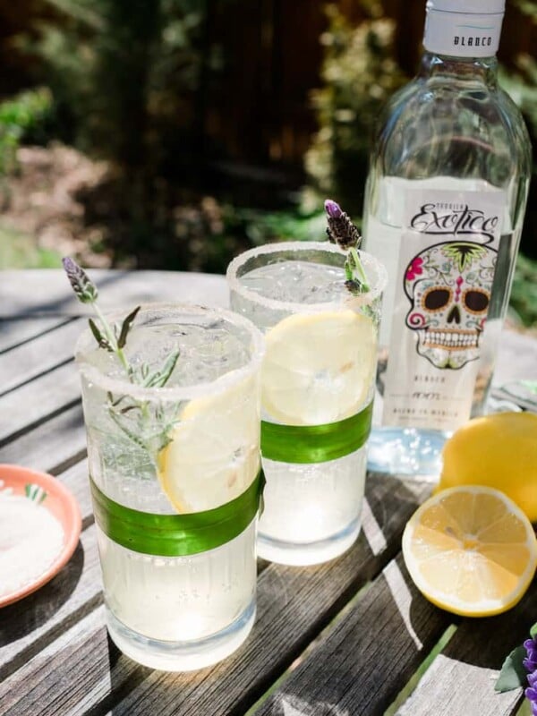 Lavender Lemon Margarita with lemons to the right and a bottle of tequila in the back