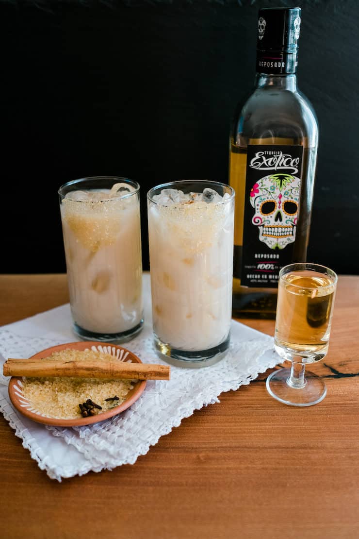 Two glasses filled with horchata and a bottle of Exotico tequila against a black background