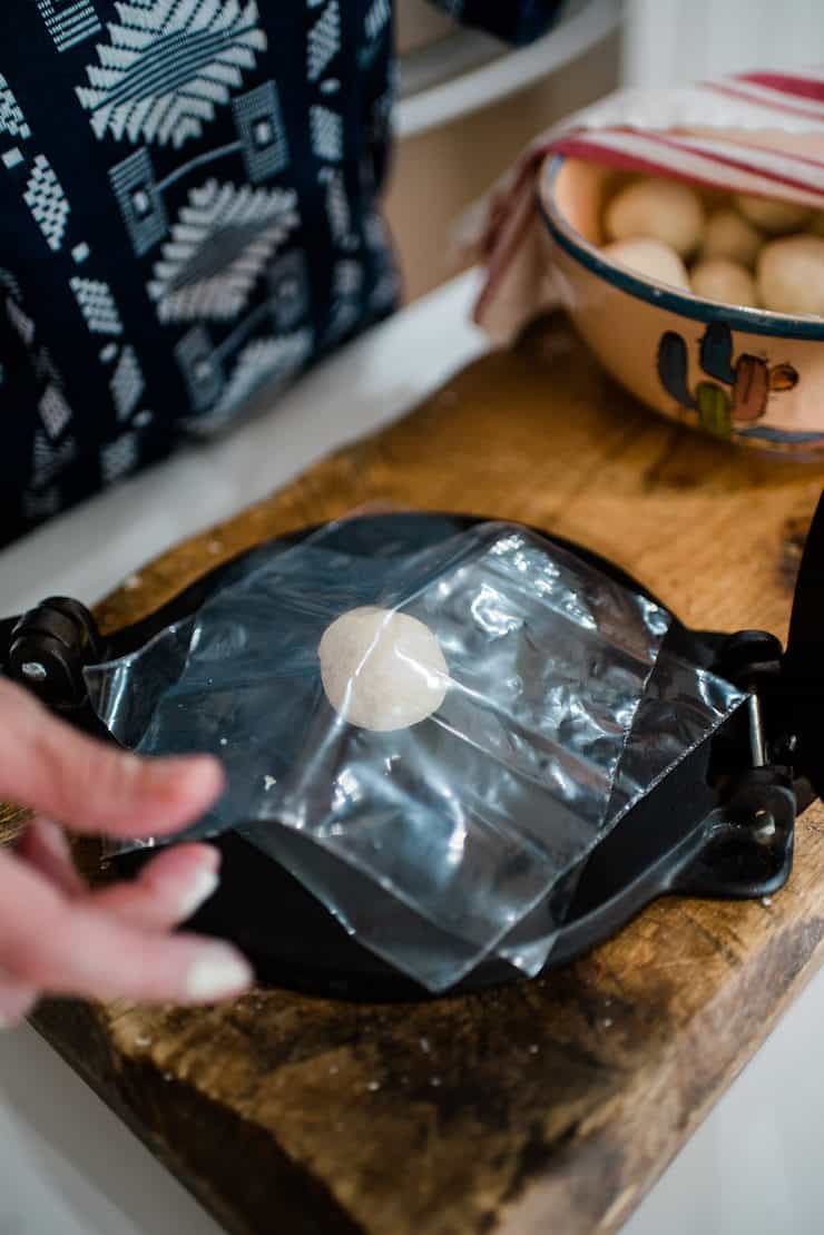 A ball of masa dough on a Tortilla Press between plastic on a big wooden board