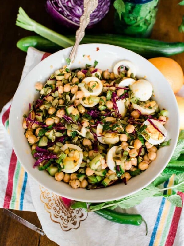 overhead shot of spicy chickpea salad with cucumbers, cilantro, and eggs in a large white serving bowl.