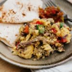 Machaca con huevo on a plate served with two flour tortillas and salsa.