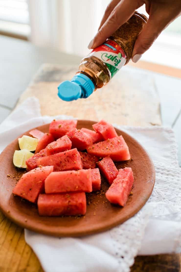 sprinkling Tajin on a plate of chopped watermelon