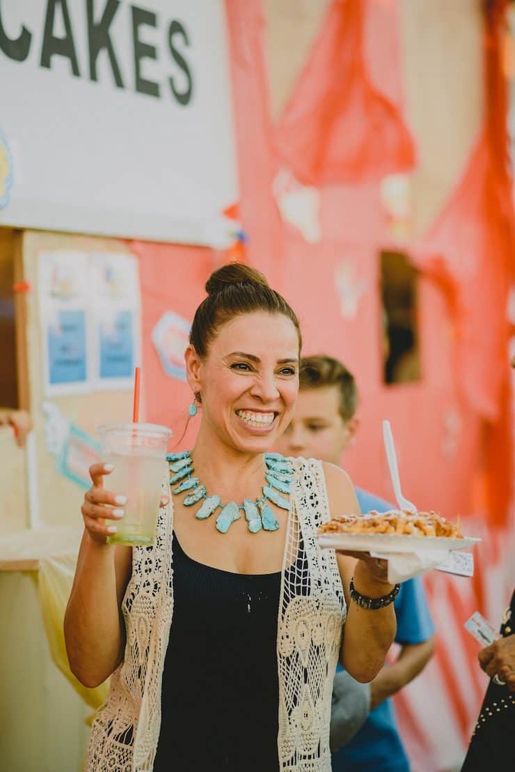 Latina food blogger at a festival holding a funnel cake and Agua Fresca 